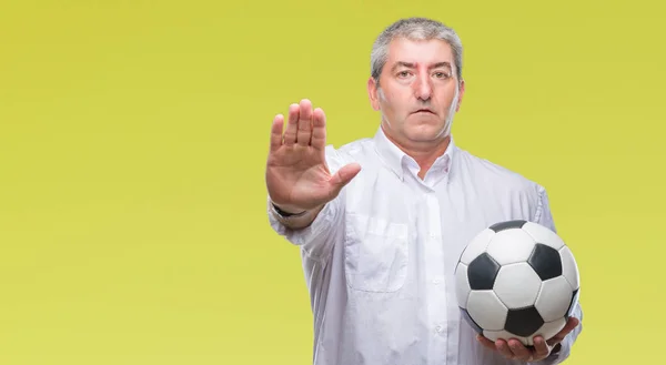 Handsome senior man holding soccer football ball over isolated background with open hand doing stop sign with serious and confident expression, defense gesture
