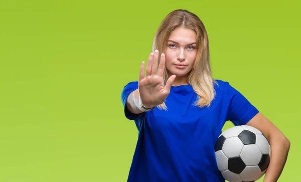 Young caucasian woman holding soccer ball over isolated background with open hand doing stop sign with serious and confident expression, defense gesture
