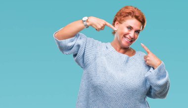 Kendinden emin gösterilen ve işaret parmakları diş ve ağız ile gülümseyen izole arka plan üzerinde kış kazak giyen Atrractive üst düzey beyaz Kızıl saçlı kadın. Sağlık kavramı.