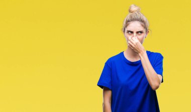 Genç güzel sarışın ve mavi gözlü kadın mavi tişört giyen bir şey pis ve iğrenç kokulu izole arka plan, dayanılmaz koku, holding nefes burun parmaklar ile. Kötü kokuyor kavramı.