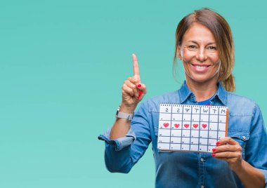 Orta yaş İspanyol kadın kıdemli holding adet izole arka bir fikirle sürpriz üzerinde takvim veya gülen yüz, bir numara ile işaret parmağı soru