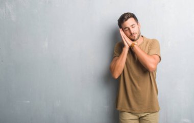 Uyku yorgun hayal ve eller ile birlikte kapalı gözlerle gülümseyerek poz gri grunge duvarın üzerinden yakışıklı genç.