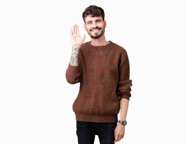 Yakışıklı delikanlı izole arka plan Waiving mutlu selam söyleyerek üzerinde kış kazak ve gülümseyen, dostça karşılama jest