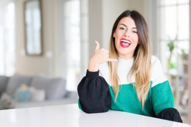 Evde kış kazak giyen genç güzel kadın gülümseyerek el ve parmak telefonda konuşmak ile telefon jest yapıyor. Kavramları iletişim.