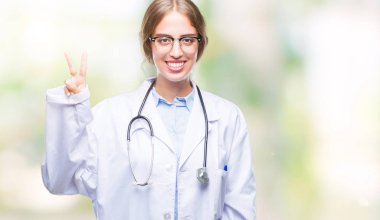 Gösterilen arka plan üzerinde tıbbi üniforma giyen güzel genç sarışın doktor kadın izole ve parmakları ile işaret kendinden emin ve mutlu gülümseyerek ise ikinci.