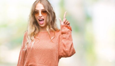 Başarılı fikirle izole arka plan işaret parmağı üzerinde güneş gözlüğü takıyor güzel sarışın genç kadın. Çıktıktan ve mutlu. Bir numara.