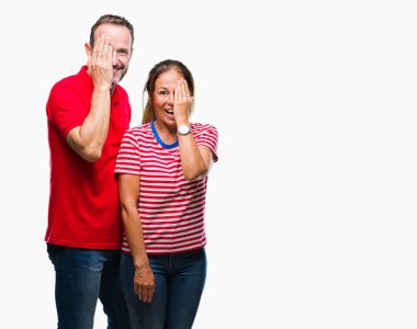 Orta yaş İspanyol çift el yüz ve sürpriz duygu kendinden emin gülümseme ile tek gözüyle kapsayan izole arka plan üzerinde aşık.