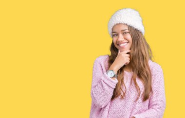 Kazak ve izole arka plan seyir üzerinde kış şapka kendinden emin çapraz kollar ve çeneme kaldırdı el ile gülümseme ile kameraya giyen genç güzel esmer kadın. Pozitif düşünce.