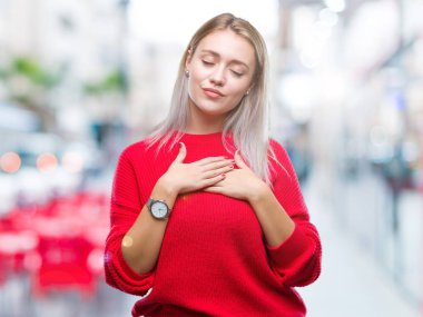 Sarışın genç kadın kapalı gözler ile göğüs ellerinde ve yüzünde minnettar jest ile gülümseyen izole arka plan üzerinde kış kazak giyiyor. Sağlık kavramı.