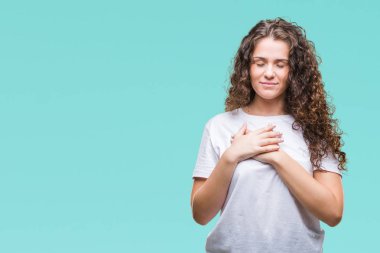 Güzel esmer kıvırcık saçlı Genç kız üzerinde gülümseyen izole arka plan ile rahat t-shirt giyen kapalı gözler ve yüzünde minnettar jest ile göğüs üzerinde eller. Sağlık kavramı.