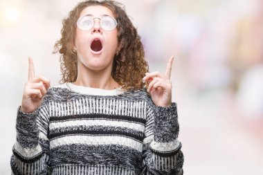 Güzel esmer kıvırcık saçlı Genç kız izole arka plan üzerinde gözlük hayret ve yukarıya bakıp parmakları ile işaret şaşırttı ve silah kaldırdı.