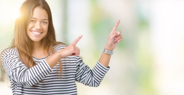 Gülümseyen ve iki elleri ve parmakları ile tarafına işaret kamera bakarak izole arka plan üzerinde çizgili süveter giyen genç güzel esmer kadın.