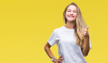 Hareketi el ile mutlu yaşasın yapıyor izole arka plan üzerinde rahat beyaz t-shirt giyen genç güzel sarışın bir kadın. Kameraya bakarak başarı gösteren ile ifade onaylama.