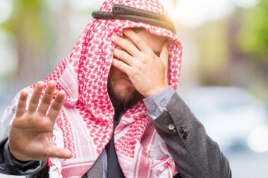 Genç yakışıklı Arap adam uzun saçlı keffiyeh üzerinde giyen izole arka plan kaplaması gözlerle eller ve üzgün dur jestle yapıyor ve korku ifadesi. Utandım ve negatif kavramı.