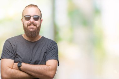 İzole arka plan mutlu yüz ile gülümseyen üzerinde güneş gözlüğü takmış Genç beyaz hipster adam kameraya seyir silah geçti. Olumlu bir kişi.