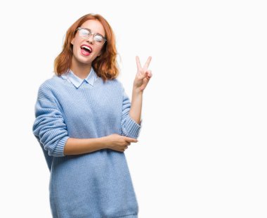 İzole arka plan mutlu yüz zafer işareti yaparken kameraya göz kırpıyor ile gülümseyen kış kazak giyen genç güzel kadın. İki numaralı.