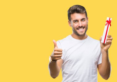 Ok işareti, başparmak ile parmak, mükemmel işareti yapıyor kocaman bir gülümseme ile izole arka plan üzerinde mutlu sevgililer günü hediyesi veren aşık genç yakışıklı adam