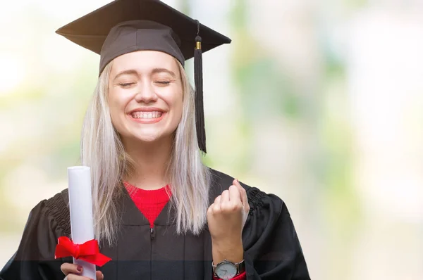 Young blonde woman wearing graduate uniform holding degree over isolated background screaming proud and celebrating victory and success very excited, cheering emotion
