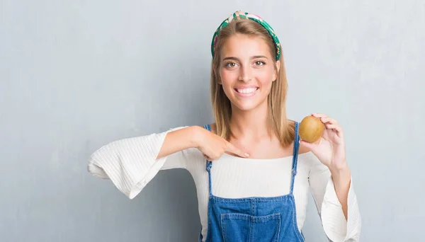 Vacker Ung Kvinna Över Grunge Grå Väggen Håller Färsk Kiwi — Stockfoto