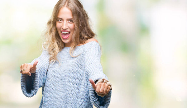 Beautiful young blonde woman wearing winter sweater over isolated background approving doing positive gesture with hand, thumbs up smiling and happy for success. Looking at the camera, winner gesture.