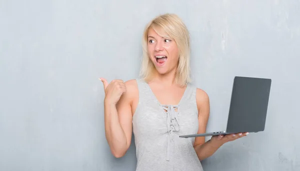 成人白种人妇女在格格灰色墙壁上使用计算机笔记本电脑指向和显示与愉快的面孔微笑的边 — 图库照片