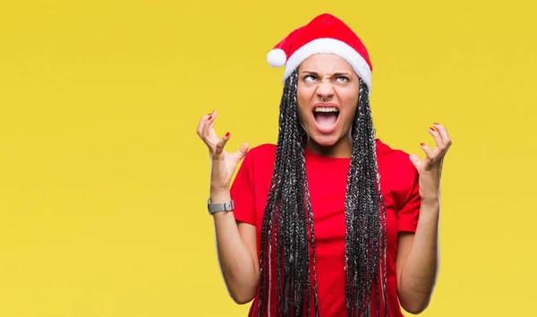 年轻的编织头发非洲裔美国女孩戴着孤立的背景圣诞帽疯狂和疯狂的喊话和大喊大叫 积极的表情和手臂抬起来 挫折的概念 — 图库照片