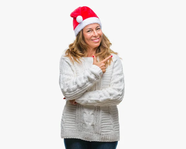 中年年配のヒスパニック系女性手と カメラ目線の顔に幸せで自然な表現のある側までの指で指している顔の笑顔で陽気な孤立の背景の上のクリスマスの帽子をかぶって — ストック写真