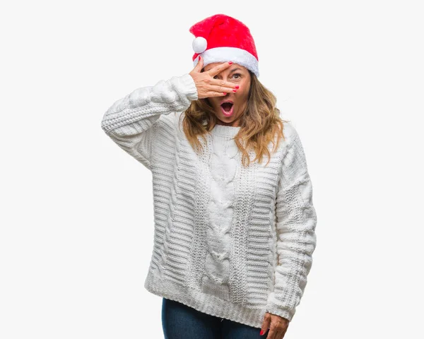 中年年配ヒスパニックの女性顔と手で目を覆うショックでピーク分離の背景をクリスマスの帽子を着て恥ずかしそうな顔で指を通して見る — ストック写真