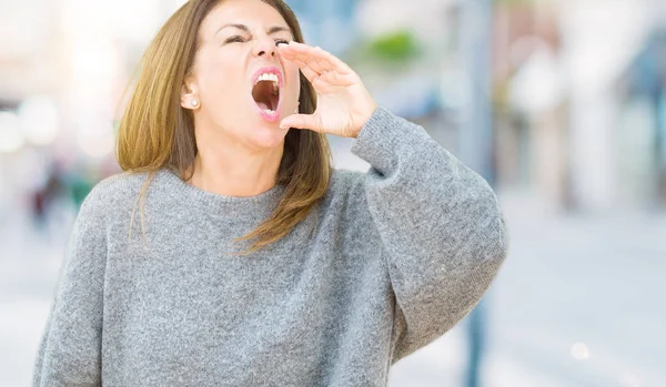 美しい中年女性が叫び 口の中に手の側に大声で叫んで孤立の背景に冬のセーターを着ています 通信の概念 — ストック写真