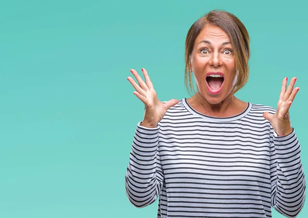 Orta yaş üst düzey İspanyol kadın deli kutluyor arka plan izole ve başarı için kaldırdı kollarını açarak hayrete ve heyecanlı çığlık gözleri açık. Kazanan kavramı