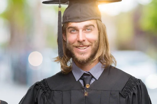 Young handsome graduated man with long hair over isolated background smiling cheerful presenting and pointing with palm of hand looking at the camera.