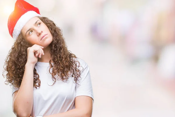 年轻的黑发女孩戴着圣诞帽在孤立的背景与手在下巴思考问题 沉思的表情 带着体贴的脸微笑 怀疑概念 — 图库照片