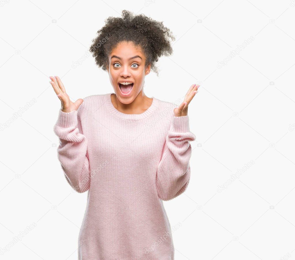 Young afro american woman wearing winter sweater over isolated background celebrating crazy and amazed for success with arms raised and open eyes screaming excited. Winner concept
