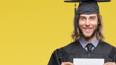 Genç yakışıklı adam uzun saçlı boş kağıt izole arka plan üzerinde duran ve diş gösterilen kendine güvenen bir gülümsemeyle gülümseyerek mutlu bir yüz ile tutarak yüksek lisans