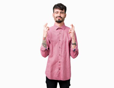 Umut ve gözleri kapalı geçiş parmaklarıyla gülümseyen izole arka plan üzerinde pembe gömlek giymiş yakışıklı delikanlı. Şans ve batıl kavramı.