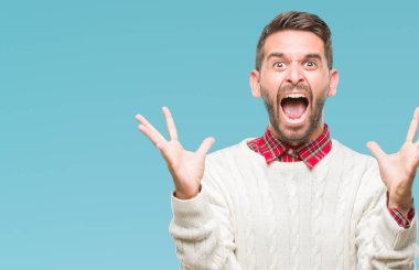 Üzerinde kış kazak giyen genç yakışıklı adam deli kutluyor arka plan izole ve başarı için kaldırdı kollarını açarak hayrete ve heyecanlı çığlık gözleri açık. Kazanan kavramı