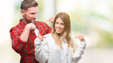 Yüzünde gülümseme ile kendinden emin görünüyorsun, kendini gururlu ve mutlu parmakları ile işaret izole arka plan üzerinde kış kazak giyen aşık genç çift.