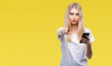 Kamera ve size parmak ile işaret arka plan üzerinde akıllı telefon kullanan genç güzel sarışın kadın izole, el işareti, pozitif ve kendinden emin bir jest ön