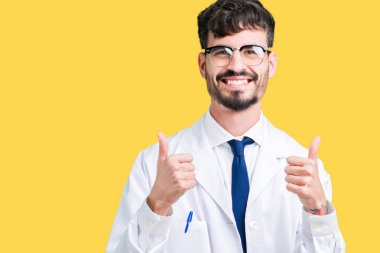 El ile pozitif jest yapıyor izole arka plan başarı işareti üzerinde beyaz önlük giyen genç profesyonel bilim adam başparmak gülümseyen ve mutlu. Neşeli bir ifadeyle, kazanan jest kameraya bakıyor.