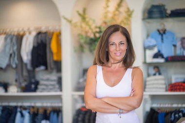 Güzel orta yaş İspanyol kadın giyim mağazasında yüzünde gülümseme ile ayakta. Dükkan sahibi ve tezgâhtar kendinden emin ve neşeli çapraz silah ile gülümseyen.