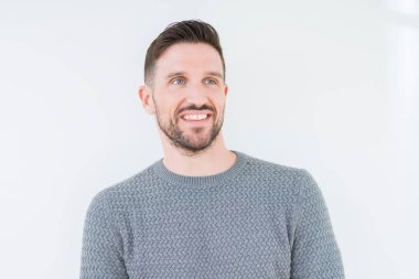 Genç yakışıklı adam uzak tarafına yüzünde, doğal ifade gülümseme ile seyir izole arka plan üzerinde rahat kazak giyiyor. Kendine güvenen gülüyor.