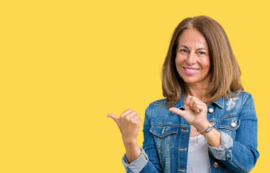 Üzerinde rahat denim ceket giyen güzel orta yaş kadın izole arka plan emin gülümseyen arkasından el ve kadar başparmak ile işaret