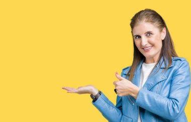 Güzel orta yaş Olgun kadın moda deri ceketin üzerinde arka plan gösteren palm el ve iş tamam jestle başparmak yukarıya, mutlu ve neşeli gülümseyen izole