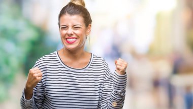 Genç güzel kadın rahat çizgili süveter üzerinde izole arka plan çok mutlu ve heyecanlı gülümseyen ve başarı için çığlık kaldırdı, silah ile kazanan jest yapıyor. Kutlama kavramı.