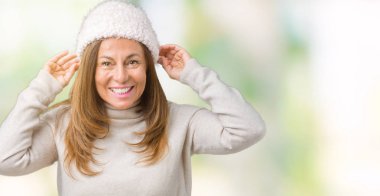 Üzerinde kış kazak ve şapka giyen güzel orta yaş kadın arka plan gülen çekerek kulakları parmaklar, komik jest ile izole. Seçmelere sorun