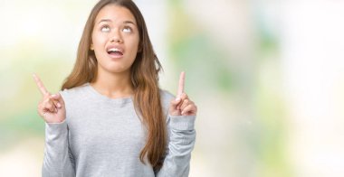 İzole arka plan üzerinde kazak giyen genç güzel esmer kadın hayrete ve yukarıya bakıp parmakları ile işaret şaşırttı ve silah kaldırdı.