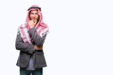 Genç yakışıklı Arap adam uzun saçlı emin çapraz kollar ve çeneme kaldırdı el ile gülümseme ile kameraya bakarak izole arka plan üzerinde keffiyeh giyiyor. Pozitif düşünce.