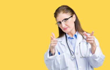 Orta yaş olgun doktor kadın kamera ile mutlu ve komik yüz için parmakları işaret izole arka plan üzerinde tıbbi bir palto giyiyor. İyi enerji ve vibes.