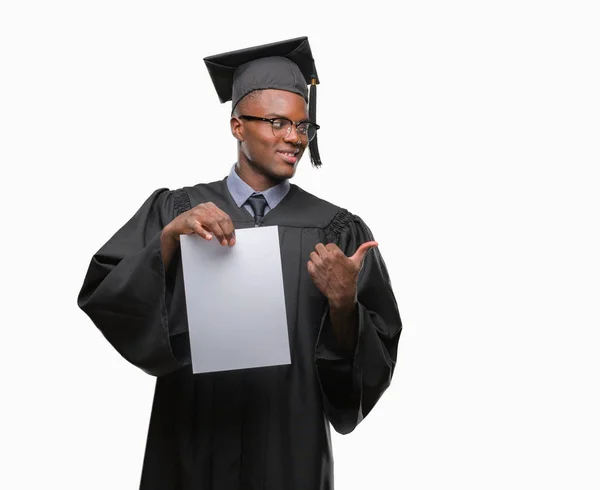 ヤング卒業したアフリカ系アメリカ人を指していると幸せそうな顔を笑顔で側まで親指で示す分離の背景に白紙の学位を保持 — ストック写真