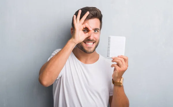 Guapo Joven Sobre Gris Pared Grunge Celebración Cuaderno Blanco Con —  Fotos de Stock